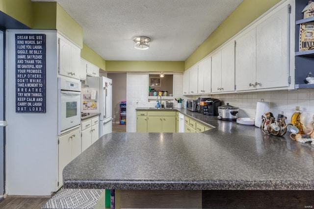 kitchen featuring white appliances, dark countertops, a peninsula, decorative backsplash, and a sink