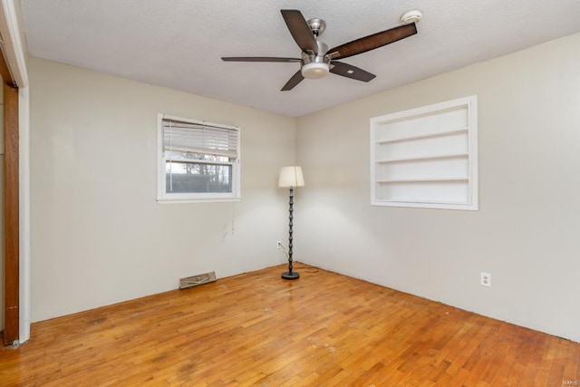 empty room featuring a ceiling fan, wood finished floors, and built in features