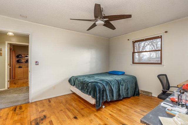 bedroom featuring wood finished floors, a textured ceiling, crown molding, ceiling fan, and baseboards