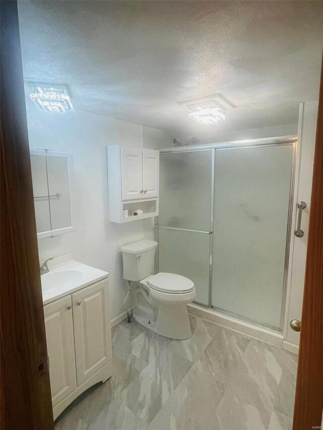 bathroom featuring a shower stall, vanity, toilet, marble finish floors, and a textured ceiling