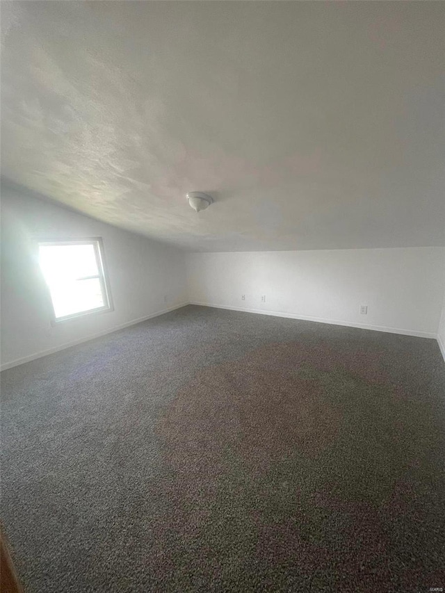 bonus room with lofted ceiling, dark carpet, and baseboards