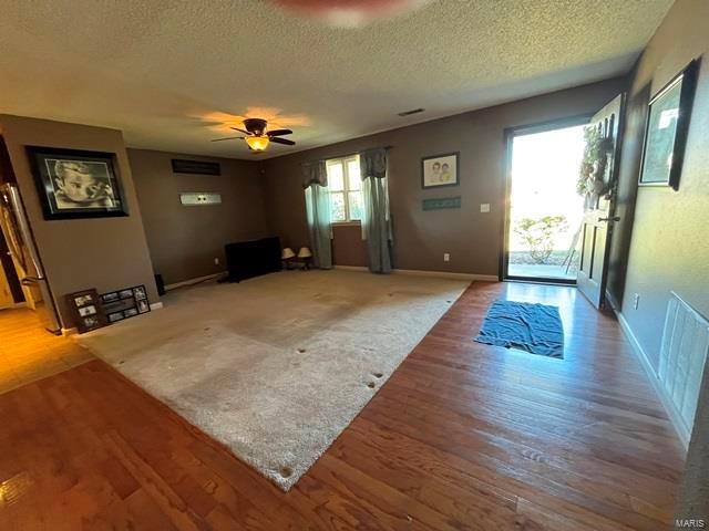 unfurnished living room with a textured ceiling, light wood-style flooring, ceiling fan, and baseboards