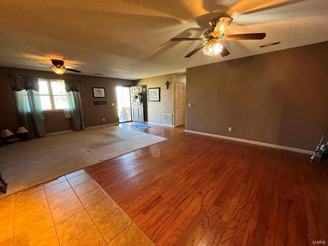 unfurnished living room with a ceiling fan, a textured ceiling, wood finished floors, carpet floors, and baseboards