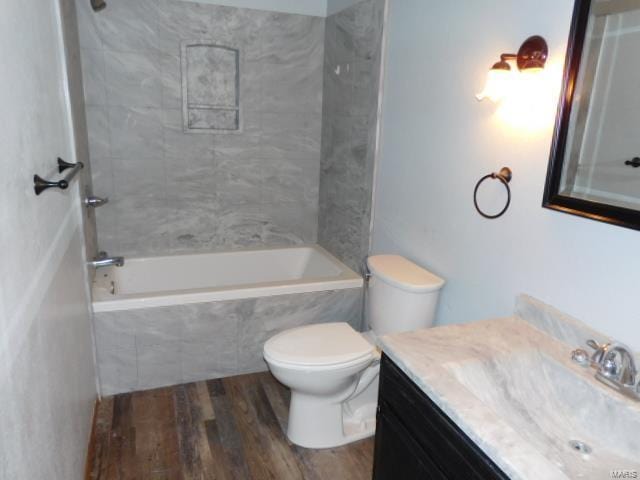 bathroom featuring wood finished floors, vanity, toilet, and tiled shower / bath