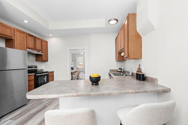 kitchen featuring stainless steel appliances, under cabinet range hood, brown cabinets, a peninsula, and light wood finished floors