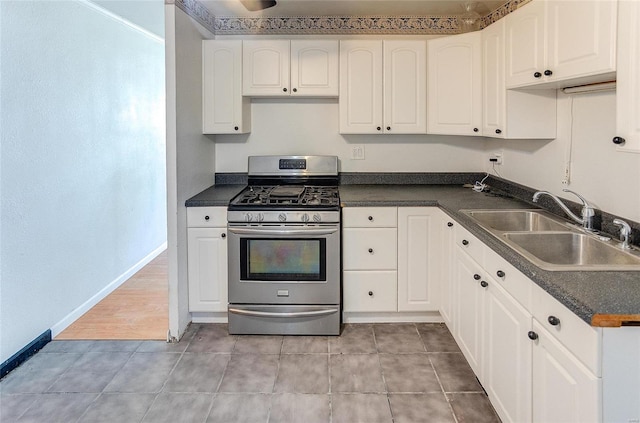 kitchen with stainless steel gas stove, a sink, dark countertops, and white cabinets