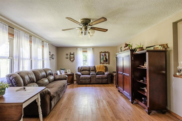 living room with a ceiling fan, light wood-type flooring, and a textured ceiling