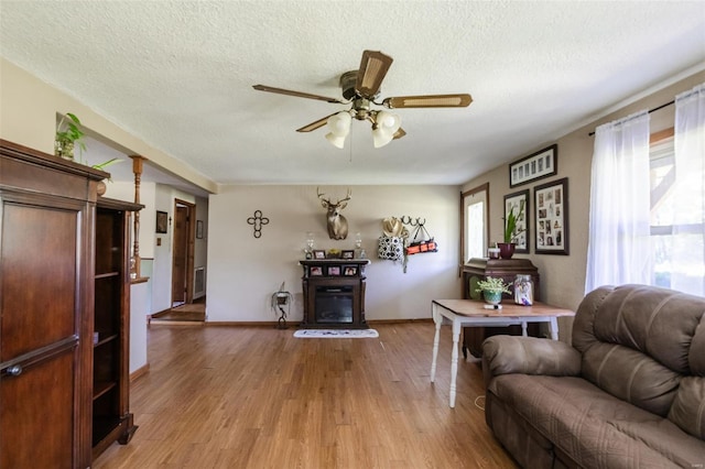 living room with healthy amount of natural light, light wood-style flooring, a ceiling fan, a textured ceiling, and baseboards