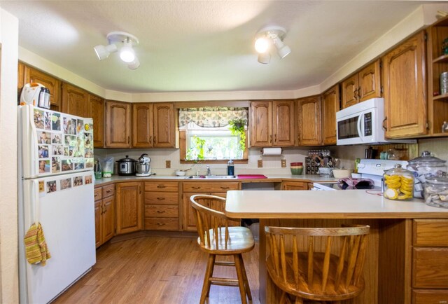 kitchen featuring white appliances, a peninsula, light countertops, and a sink