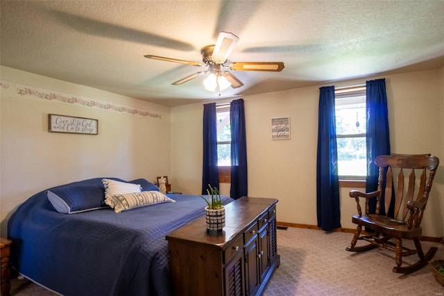 bedroom featuring multiple windows, a textured ceiling, ceiling fan, baseboards, and light colored carpet