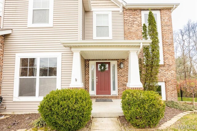 view of exterior entry featuring brick siding and covered porch