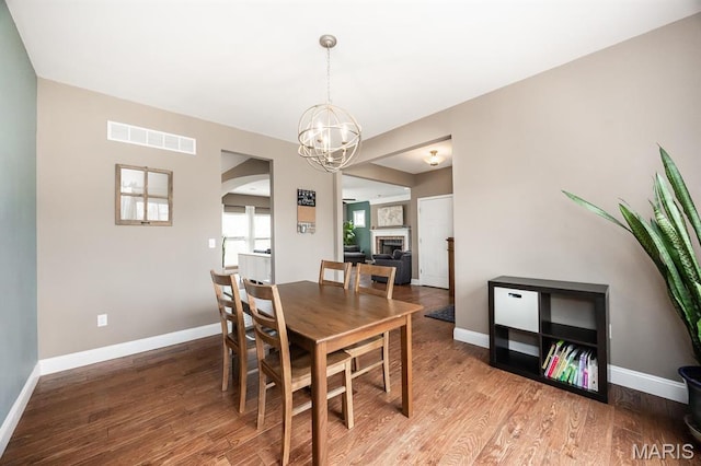dining space with a chandelier, arched walkways, wood finished floors, and baseboards