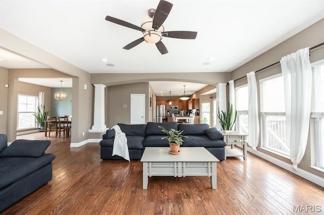 living area featuring decorative columns, arched walkways, wood finished floors, baseboards, and ceiling fan