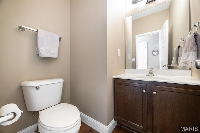 half bathroom featuring baseboards, wood finished floors, vanity, and toilet