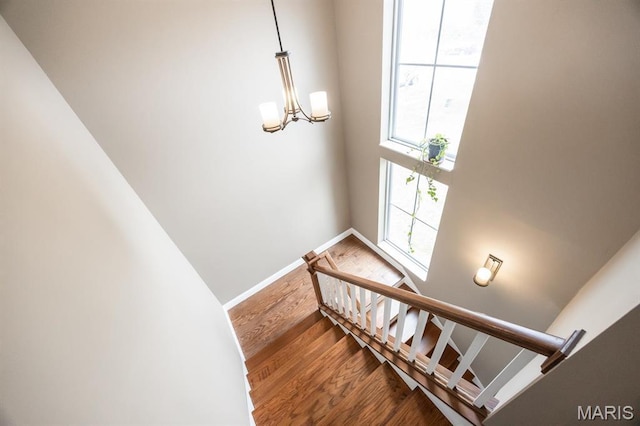 stairway featuring wood finished floors, a chandelier, and baseboards