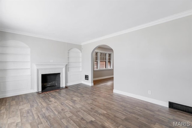 unfurnished living room featuring built in shelves, baseboards, ornamental molding, wood finished floors, and a fireplace