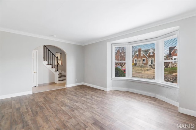 spare room with arched walkways, wood finished floors, stairs, crown molding, and baseboards