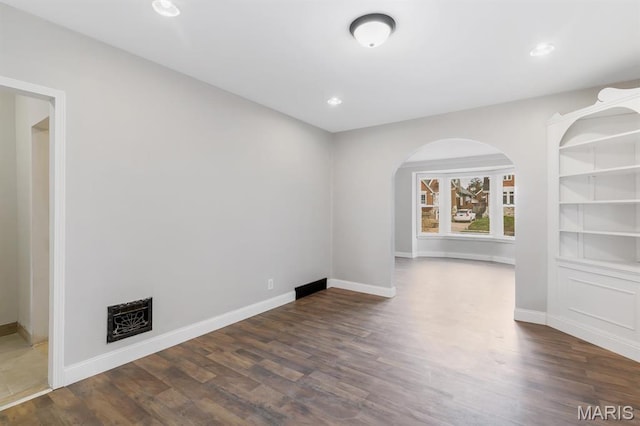 unfurnished room with dark wood-type flooring, baseboards, arched walkways, and recessed lighting