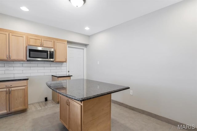 kitchen with stainless steel microwave, dark stone countertops, tasteful backsplash, a kitchen island, and light tile patterned flooring
