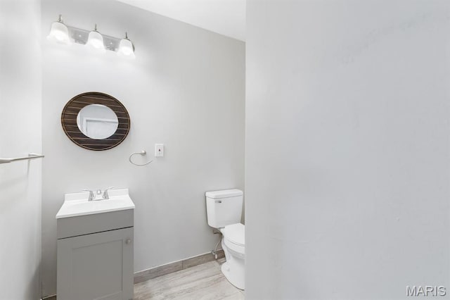 half bathroom with toilet, vanity, wood finished floors, and baseboards