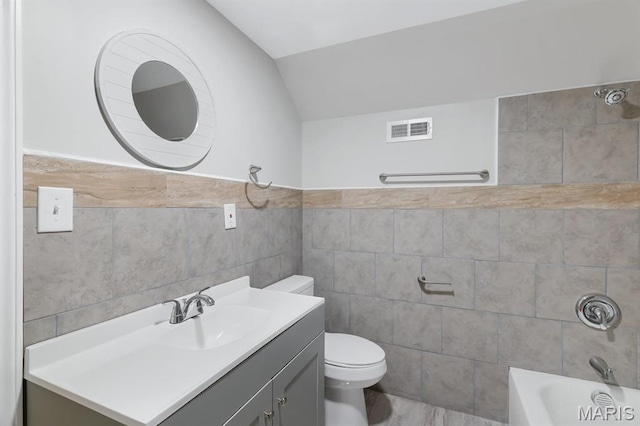 bathroom featuring tile walls, toilet, lofted ceiling, vanity, and bathtub / shower combination