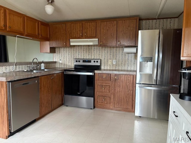 8336 Cedar Fork Rd, New Haven, MO 63068 - kitchen with appliances with stainless steel finishes, a sink, under cabinet range hood, brown cabinetry, and wallpapered walls