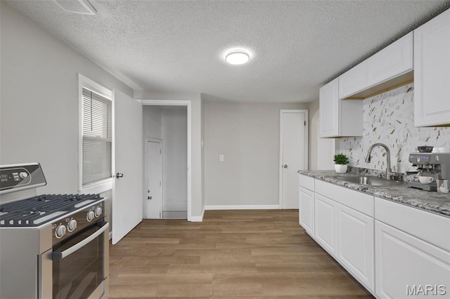 9515 Edmund Ave, Saint Louis, MO 63114 - kitchen with gas stove, light wood-type flooring, tasteful backsplash, white cabinets, and a textured ceiling