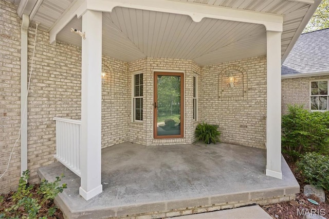 entrance to property featuring covered porch, brick siding, and a shingled roof