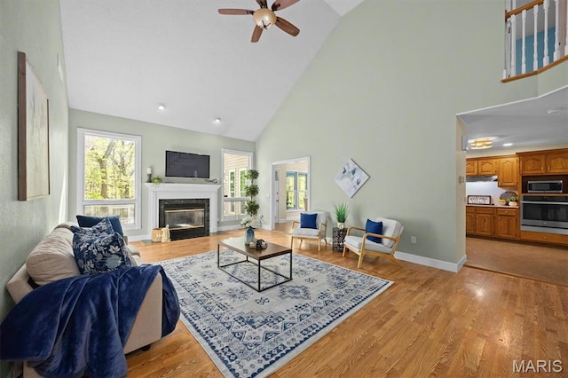 living area featuring high vaulted ceiling, a ceiling fan, plenty of natural light, a high end fireplace, and light wood-type flooring