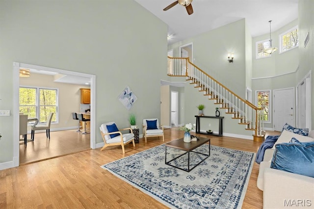 living area featuring a high ceiling, stairway, wood finished floors, ceiling fan, and baseboards