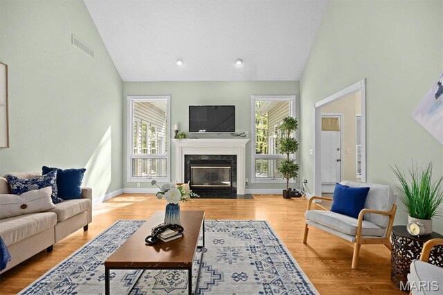 living room featuring high vaulted ceiling, a high end fireplace, wood finished floors, and baseboards