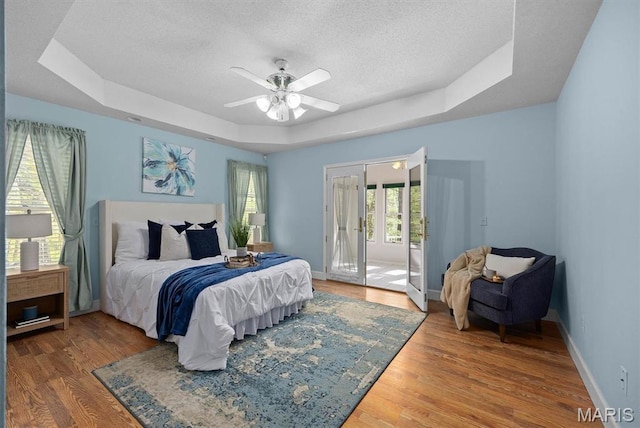 bedroom with a tray ceiling, a textured ceiling, wood finished floors, access to exterior, and baseboards