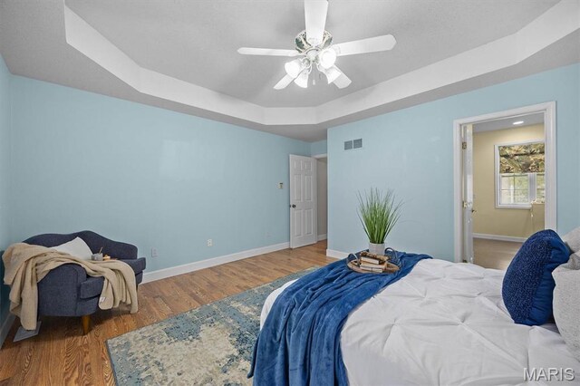 bedroom featuring a tray ceiling, baseboards, wood finished floors, and ceiling fan