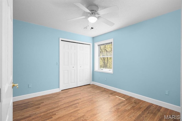 unfurnished bedroom with a closet, a textured ceiling, wood finished floors, baseboards, and a ceiling fan
