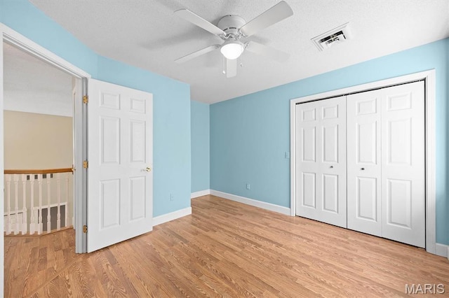 unfurnished bedroom featuring light wood-type flooring, a closet, baseboards, a ceiling fan, and a textured ceiling