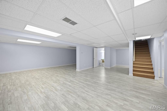finished basement with stairway, wood finished floors, baseboards, and a paneled ceiling