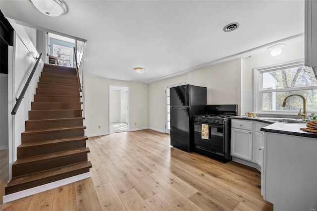 1300 Hudson Rd, Saint Louis, MO 63135 - kitchen with black appliances, a sink, light wood-style floors, dark countertops, and white cabinets