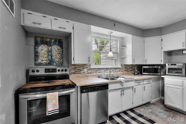 kitchen featuring appliances with stainless steel finishes, a sink, light countertops, white cabinets, and decorative backsplash
