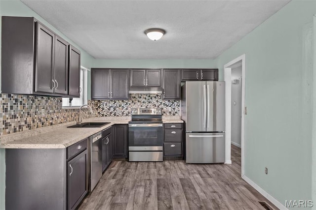 953 E 1st St, Washington, MO 63090 - kitchen featuring appliances with stainless steel finishes, a sink, under cabinet range hood, decorative backsplash, and wood finished floors