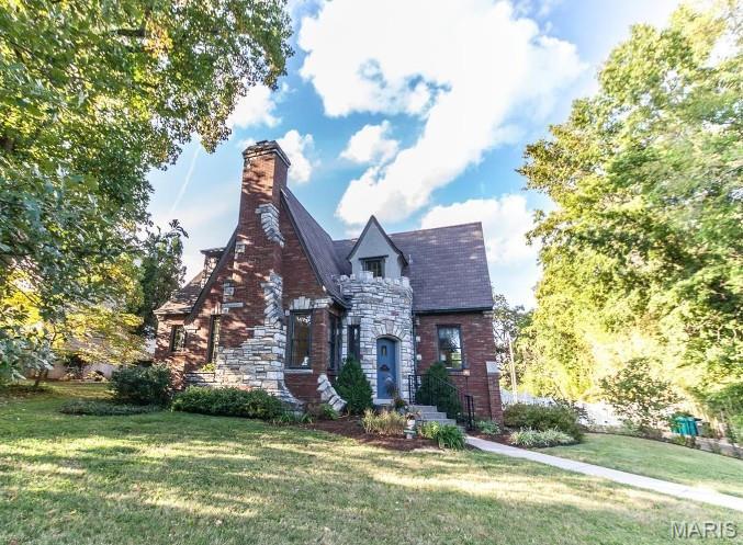 tudor-style house featuring a front yard, stone siding, and a chimney