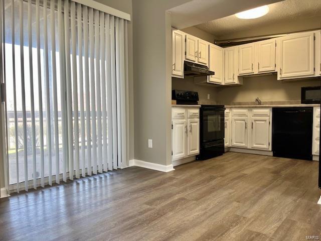 1767 High School Dr, Brentwood, MO 63144 - kitchen with black appliances, under cabinet range hood, light wood finished floors, baseboards, and white cabinets