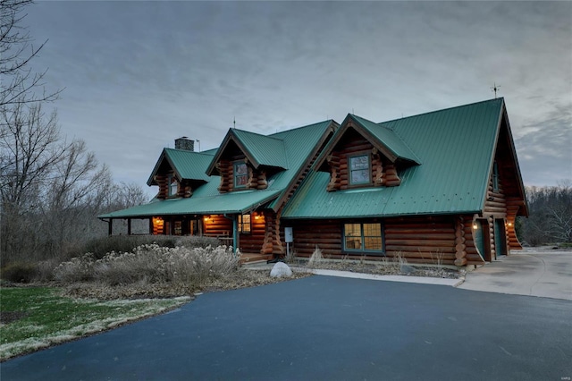 log-style house featuring log exterior, a chimney, covered porch, metal roof, and a garage