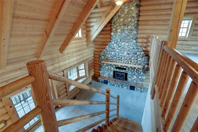 stairway featuring rustic walls, beamed ceiling, healthy amount of natural light, wooden ceiling, and a stone fireplace