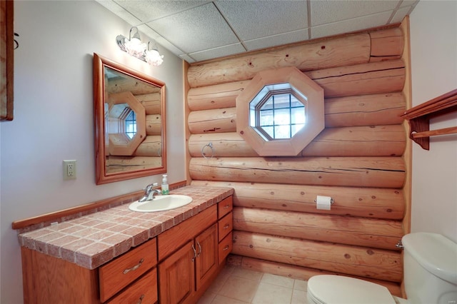 half bathroom featuring rustic walls, toilet, a paneled ceiling, vanity, and tile patterned flooring