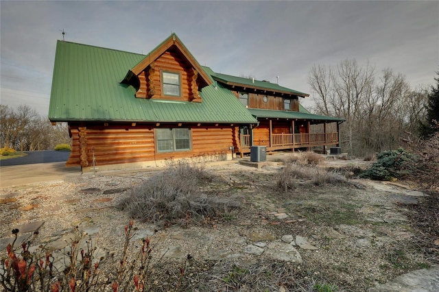 log-style house with log siding, metal roof, central AC unit, and a porch