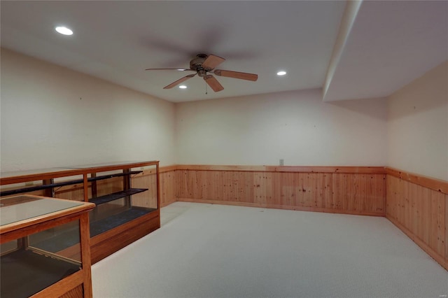 unfurnished office featuring light colored carpet, wainscoting, wood walls, recessed lighting, and a ceiling fan