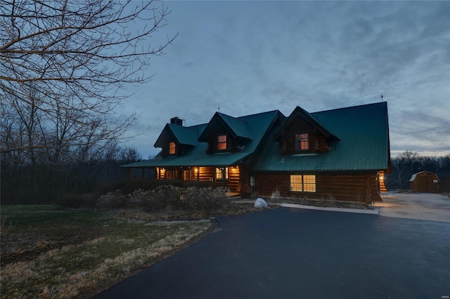 log-style house with log siding, a chimney, covered porch, and asphalt driveway