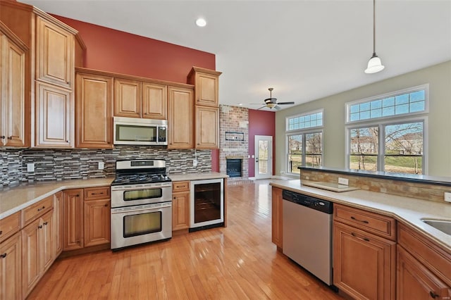 2707 Fairway Estates Dr, Wentzville, MO 63385 - kitchen with appliances with stainless steel finishes, wine cooler, a ceiling fan, a brick fireplace, and light wood-type flooring