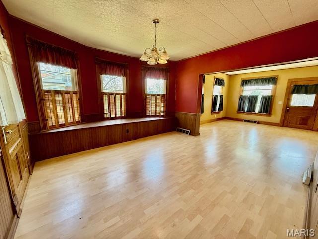 201 W Barr Ave, Jerseyville, IL 62052 - unfurnished dining area with a chandelier, wainscoting, light wood-style flooring, and a textured ceiling