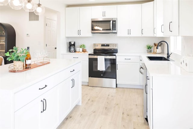 407 Front St, Monroe City, MO 63456 - kitchen featuring appliances with stainless steel finishes, a sink, light countertops, light wood finished floors, and white cabinetry